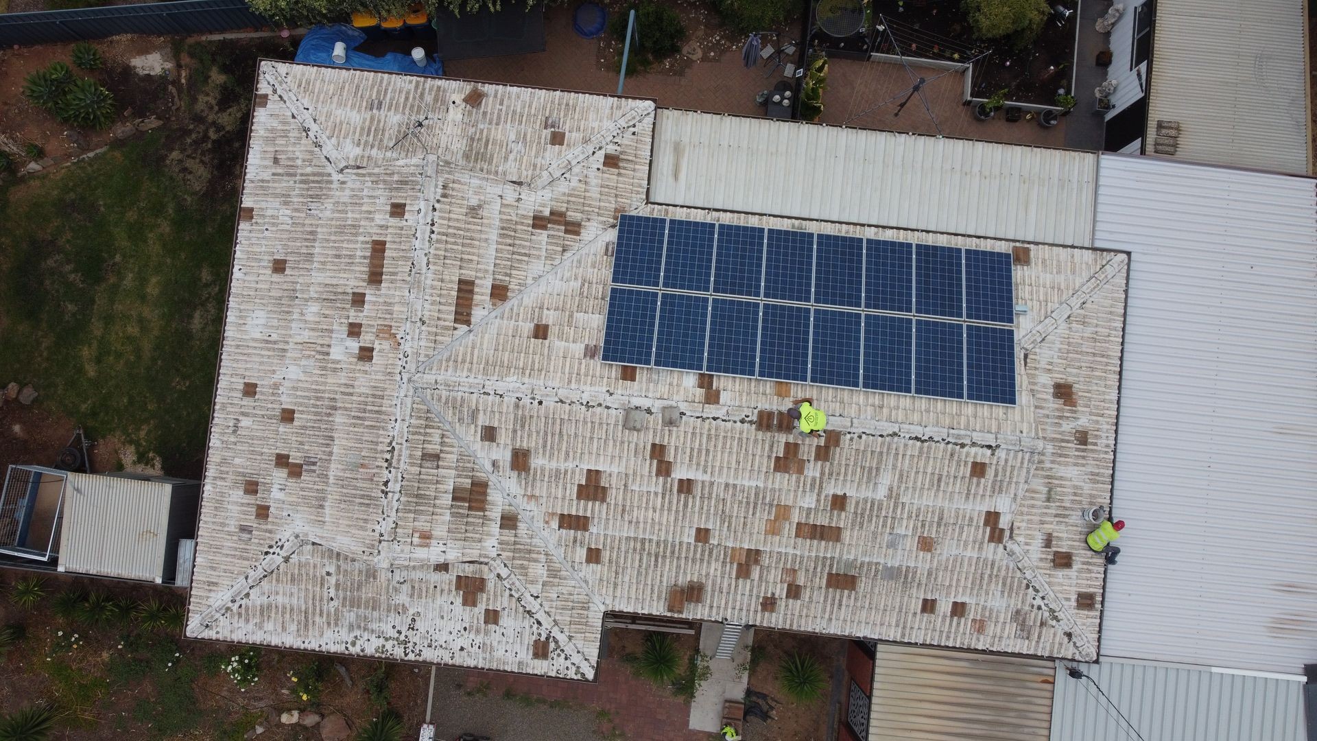 Aerial view of a roof with solar panels and two workers in yellow vests.